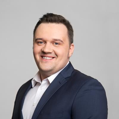 Portret mężczyzny w garniturze i białej koszuli, uśmiechnięty, na jasnym tle, zdjęcie biznesowe do profilu firmowego.