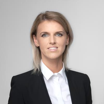 Portret biznesowy kobiety w czarnej marynarce i białej koszuli na jasnym tle.