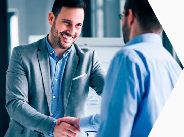 Dwóch mężczyzn ubranych w koszule i marynarki podających sobie ręce podczas spotkania biznesowego.