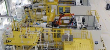 Zautomatyzowana linia produkcyjna w hali przemysłowej z żółtymi platformami bezpieczeństwa oraz robotem przemysłowym.