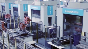 Zautomatyzowana linia obróbcza w hali przemysłowej z centrami CNC i robotami przemysłowymi, oddzielona barierami bezpieczeństwa.