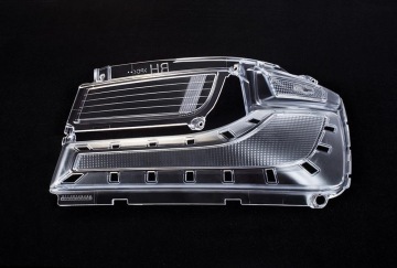 Przezroczysty plastikowy element lampy samochodowej z widoczną strukturą wewnętrzną, na czarnym tle.