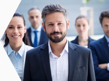 Mężczyzna w garniturze wraz z wspólpracownikami w biznesowych strojach, którzy stoją za nim. Wszyscy znajdują się w jasnym wnętrzu.