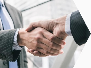 Zbliżenie na uścisk dłoni dwóch osób w garniturach w nowoczesnym wnętrzu biurowym.