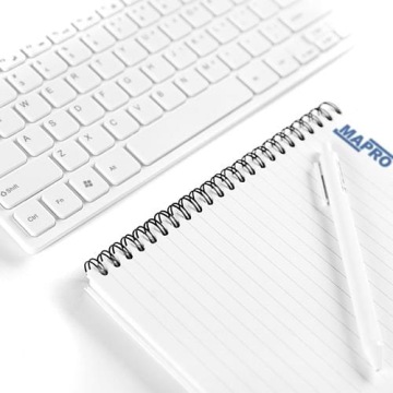 Biała klawiatura komputerowa oraz notes spiralny z logo MAPRO i długopisem.