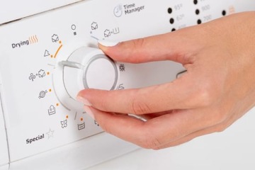 Dłoń osoby ustawiającej program prania lub suszenia za pomocą pokrętła na białym panelu sterowania urządzenia AGD.