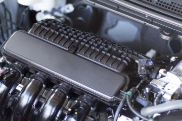 Zbliżenie na komorę silnika samochodu – widoczna czarna obudowa filtra powietrza oraz elementy układu dolotowego i przewody.