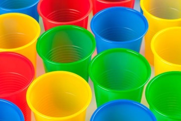 Kolorowe plastikowe kubki jednorazowe w kolorach żółtym, zielonym, niebieskim i czerwonym, ustawione obok siebie.