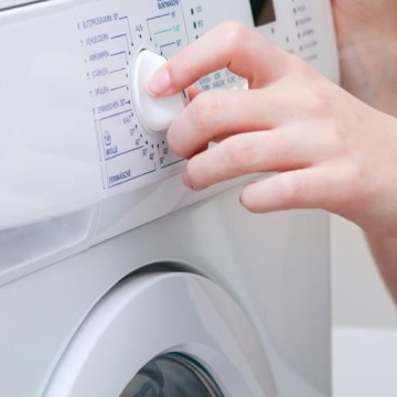 Dłoń ustawiająca program prania na panelu pralki.