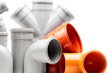 Kształtki i rury z tworzywa sztucznego w kolorze szarym i pomarańczowym, stosowane w instalacjach kanalizacyjnych i sanitarnych.