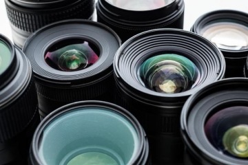 Zbliżenie na kilka obiektywów fotograficznych ułożonych obok siebie, widoczne soczewki z refleksami światła.
