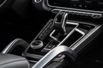 Wnętrze nowoczesnego samochodu – centralny tunel z automatyczną dźwignią zmiany biegów, pokrętłem sterowania i przyciskami funkcji.