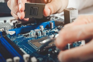 Zbliżenie na dłonie montujące procesor w gnieździe płyty głównej komputera; widoczne elementy elektroniki i slot procesora.