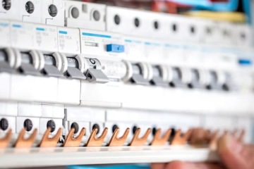 Rozdzielnica elektryczna z zamontowanymi wyłącznikami nadprądowymi oraz miedzianą szyną widok z bliska podczas montażu lub serwisu.