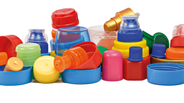 Stos różnorodnych kolorowych plastikowych nakrętek, kapsli i wieczek do butelek, ułożonych w chaotyczną kupę na białym tle.