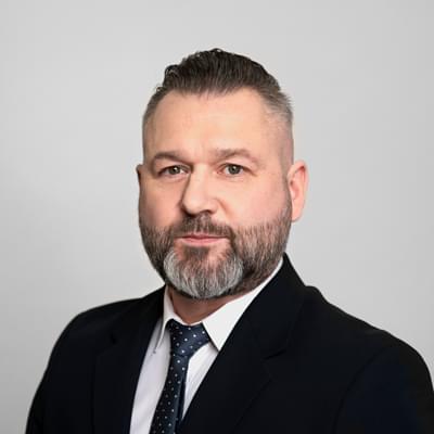 Biznesowy portret mężczyzny w ciemnym garniturze i krawacie na jasnym tle.