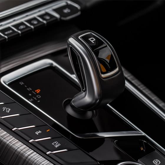 Dźwignia automatycznej skrzyni biegów w luksusowym samochodzie, widoczny podświetlany panel oraz przyciski trybów jazdy i parkowania.